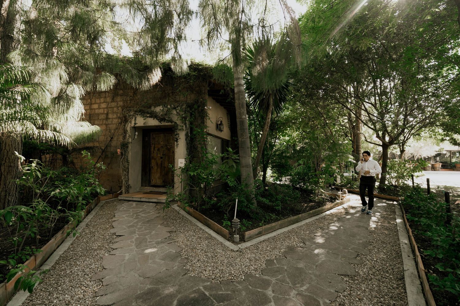 Stone pathway leading to rustic doorway surrounded by tropical greenery.