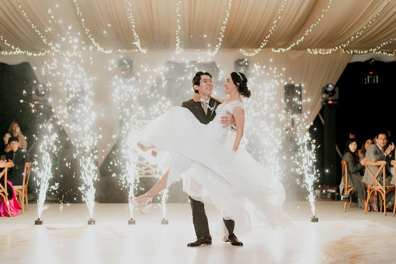 Sparkling fountains create a magical atmosphere during a wedding first dance under white tent draping.