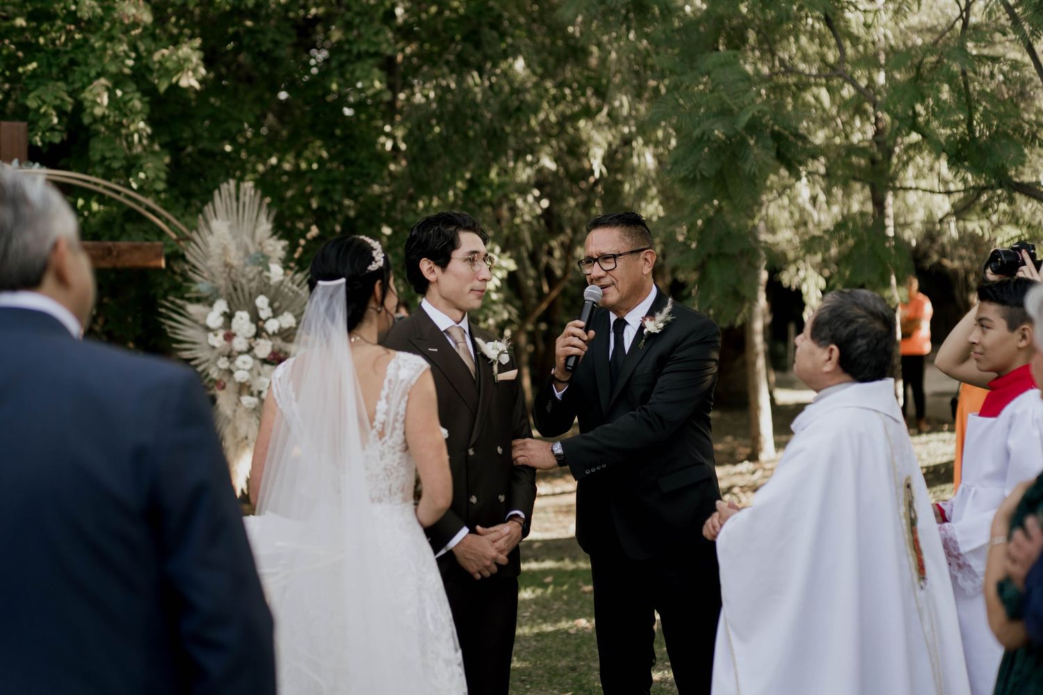 Elegant outdoor wedding ceremony with guests gathered under trees.
