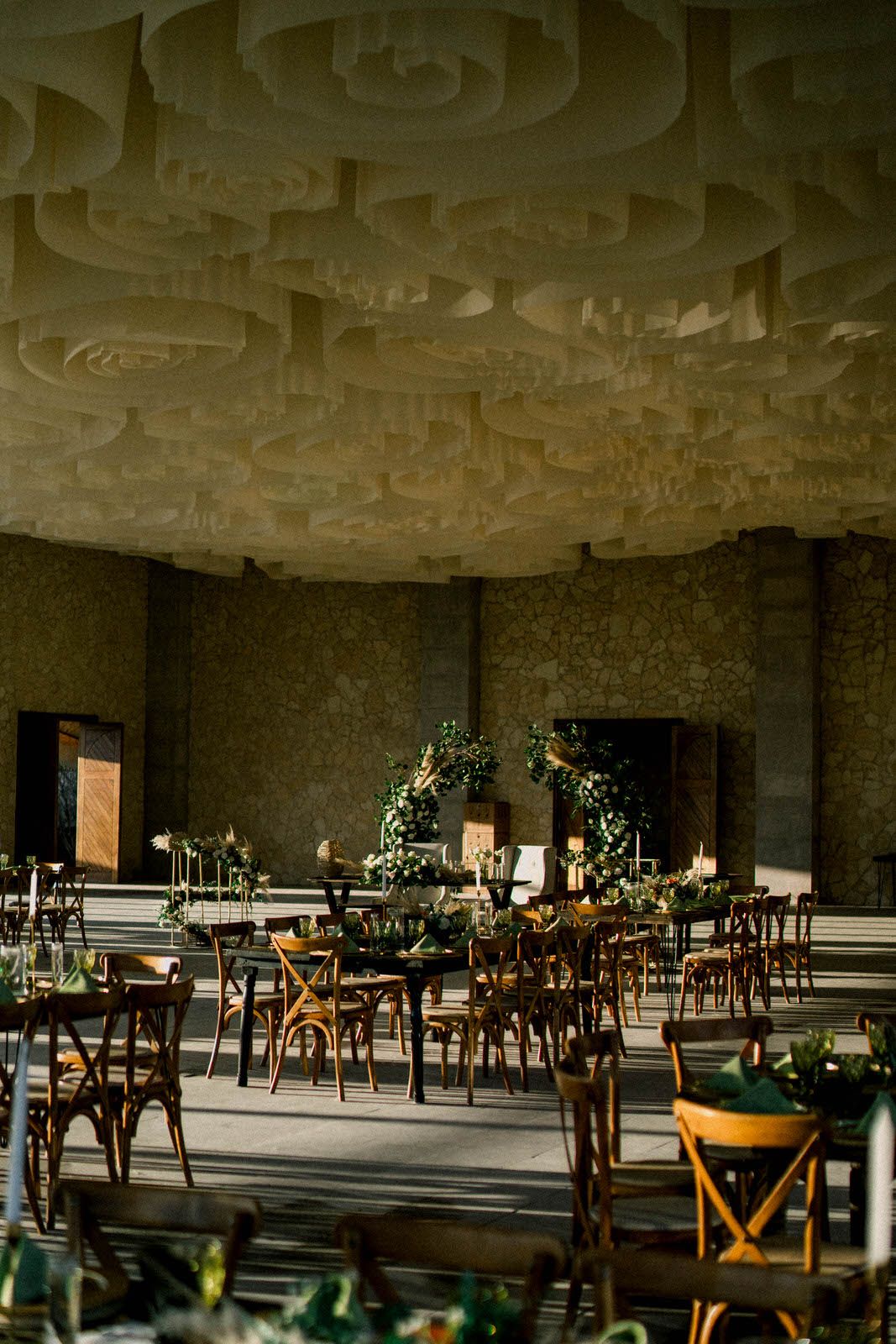 Elegant wedding venue interior with wooden cross-back chairs and ornate ceiling details.