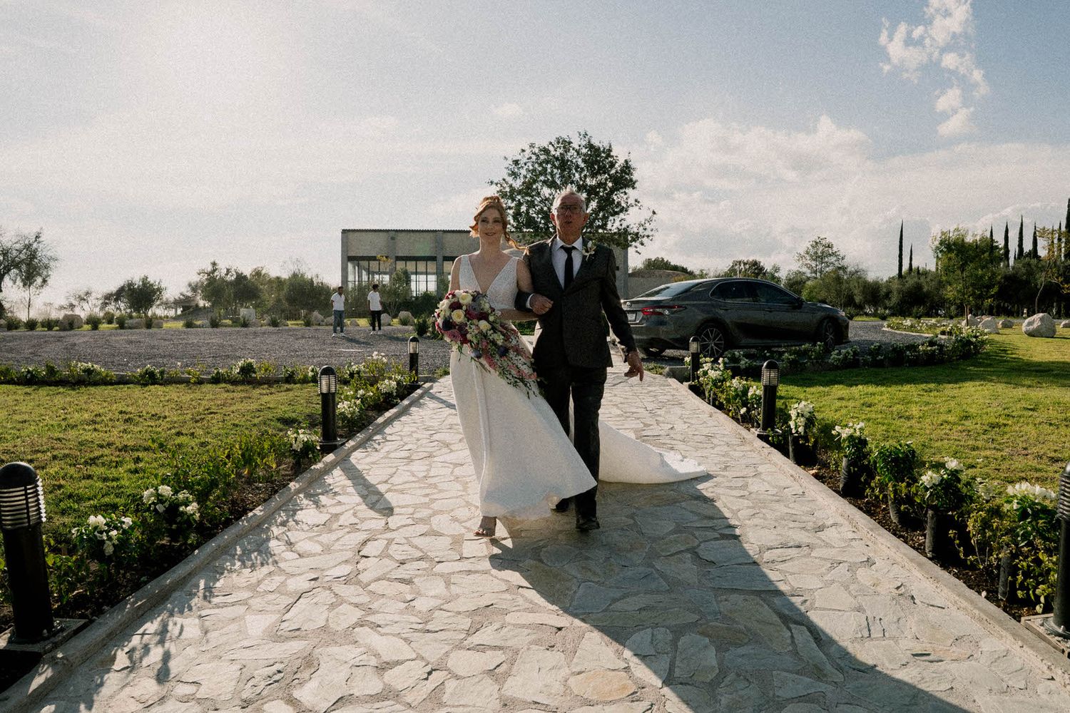 Wedding ceremony guests gather under a wooden pergola with stone flooring and scenic landscape views.