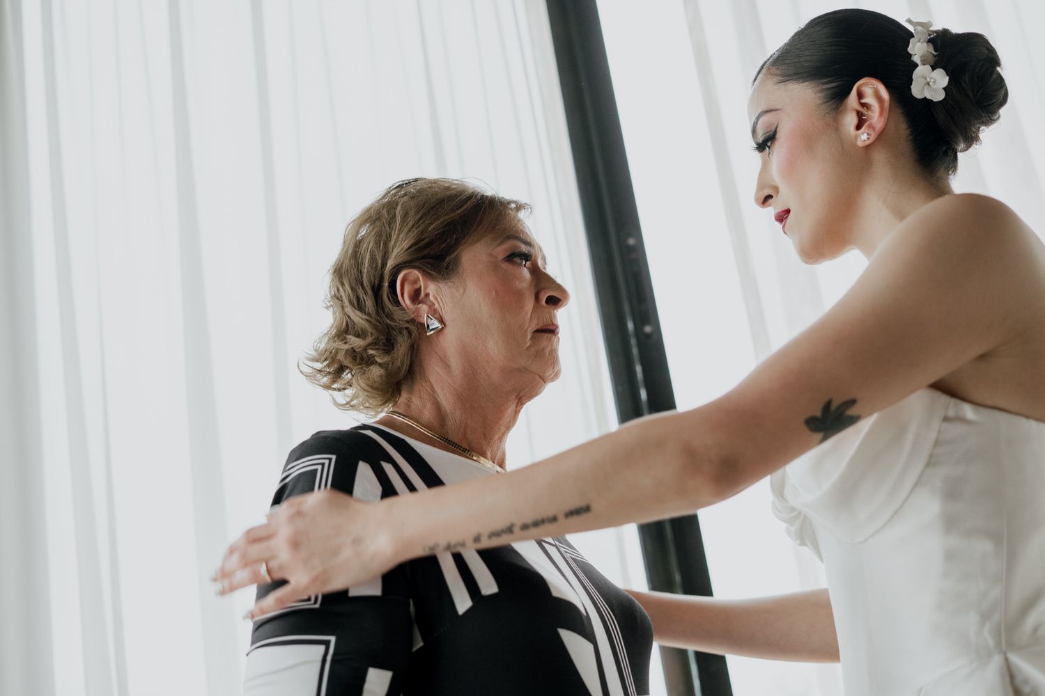 An intimate moment during wedding preparations near white curtained windows.