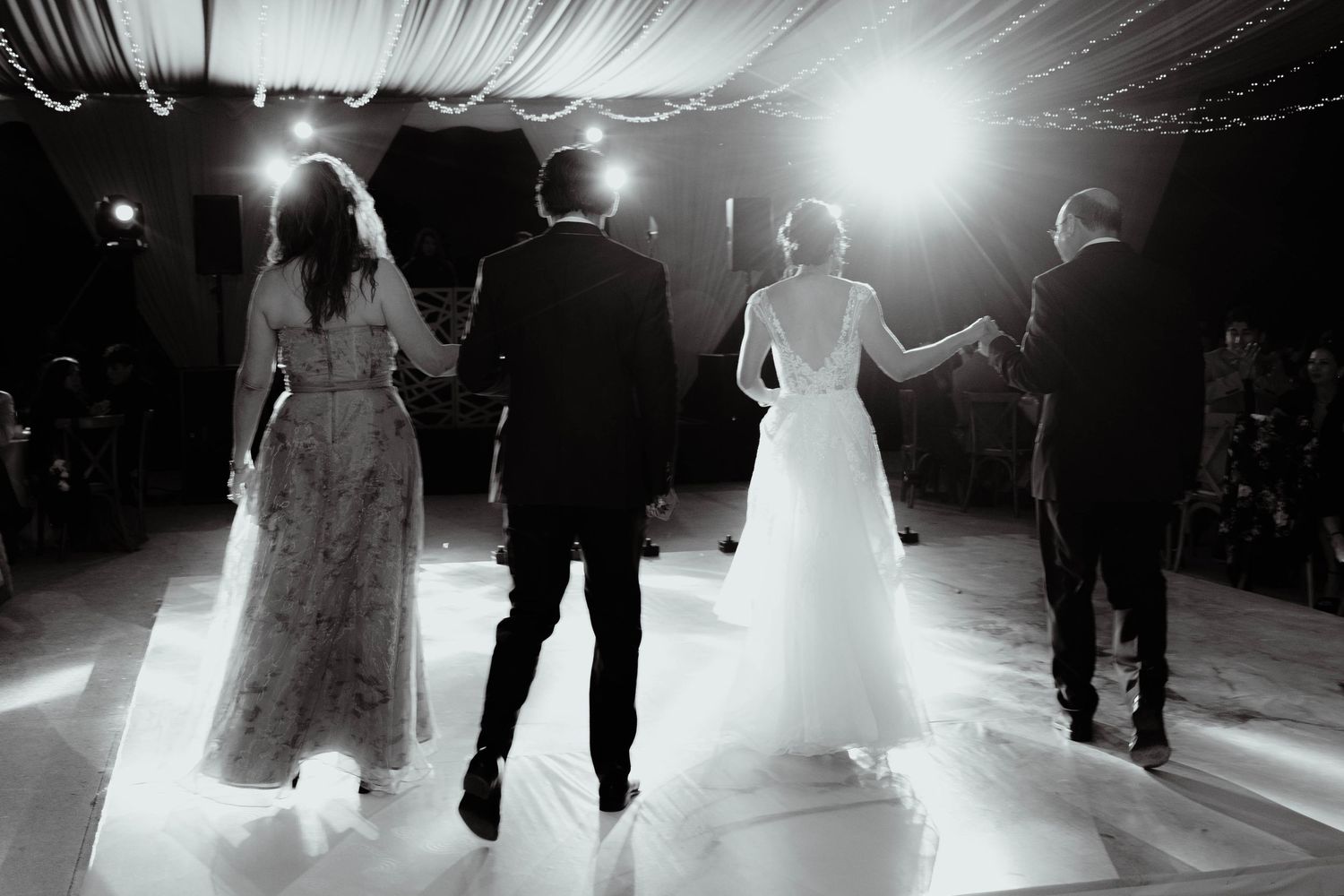 Dramatic black and white shot of wedding dance floor with silhouettes and string lights.