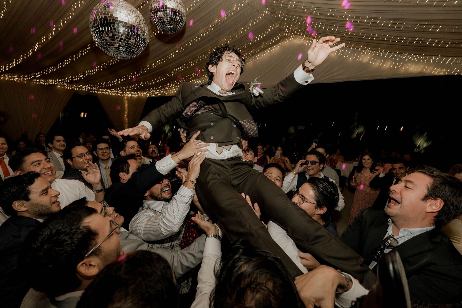 Wedding party dancing and celebrating beneath twinkling lights and disco balls at reception.