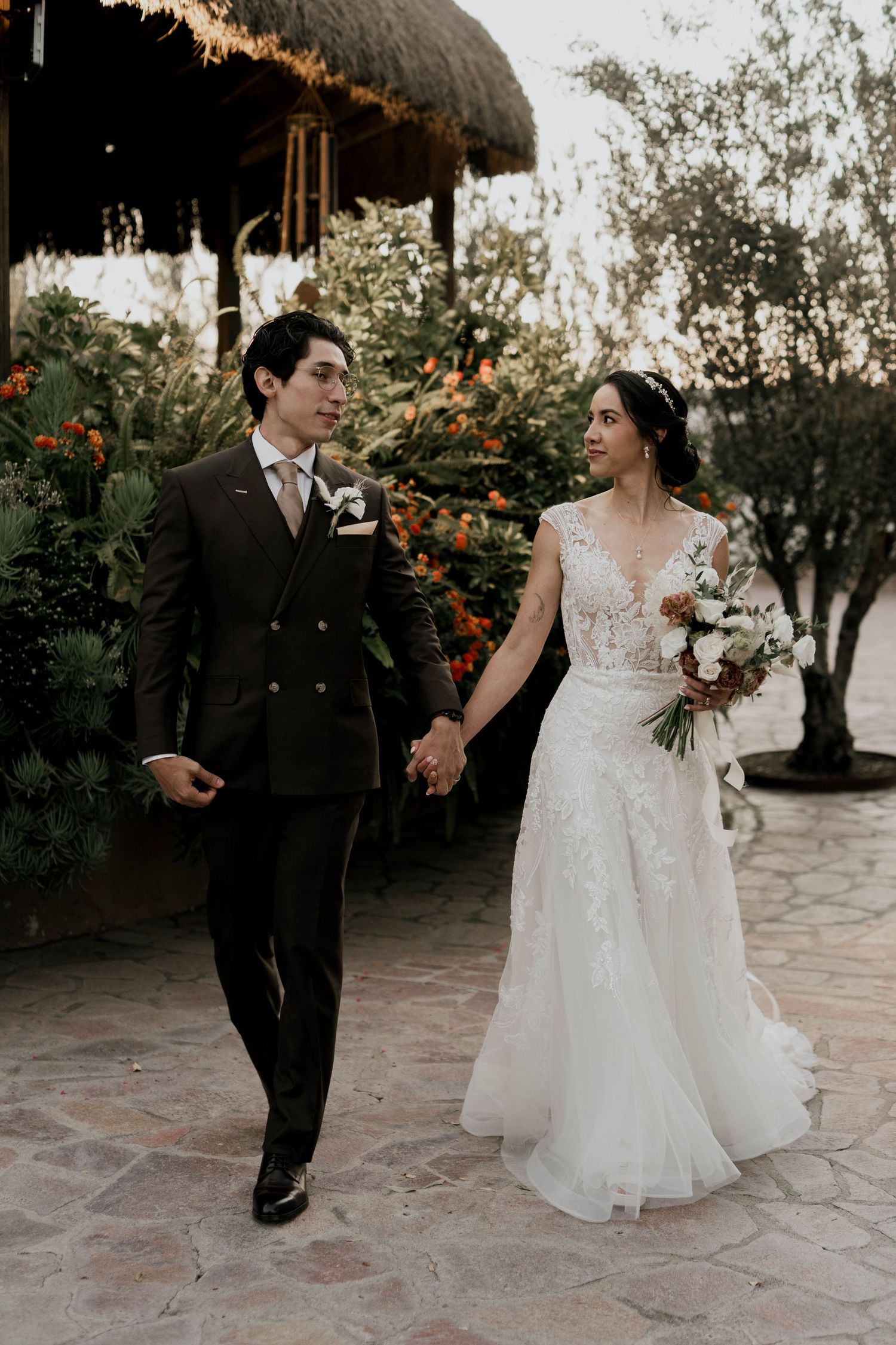 Wedding couple walking and dancing on stone patio surrounded by tropical plants.