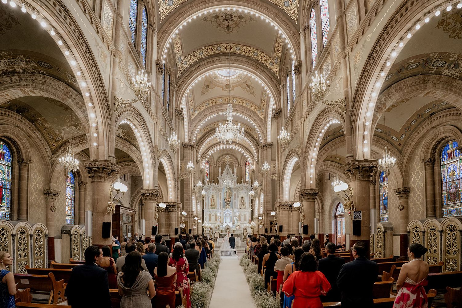 Grand cathedral wedding ceremony with ornate arched ceilings, stained glass windows, and guests filling pews.