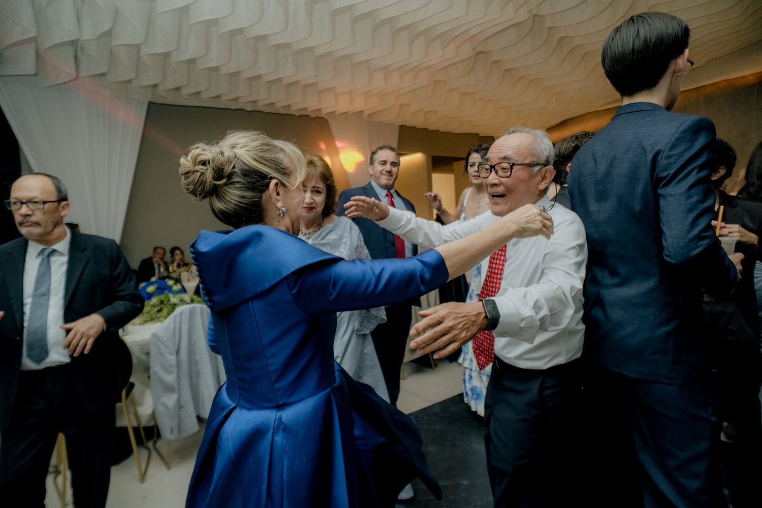Guests dancing and embracing joyfully at elegant wedding reception in formal attire.