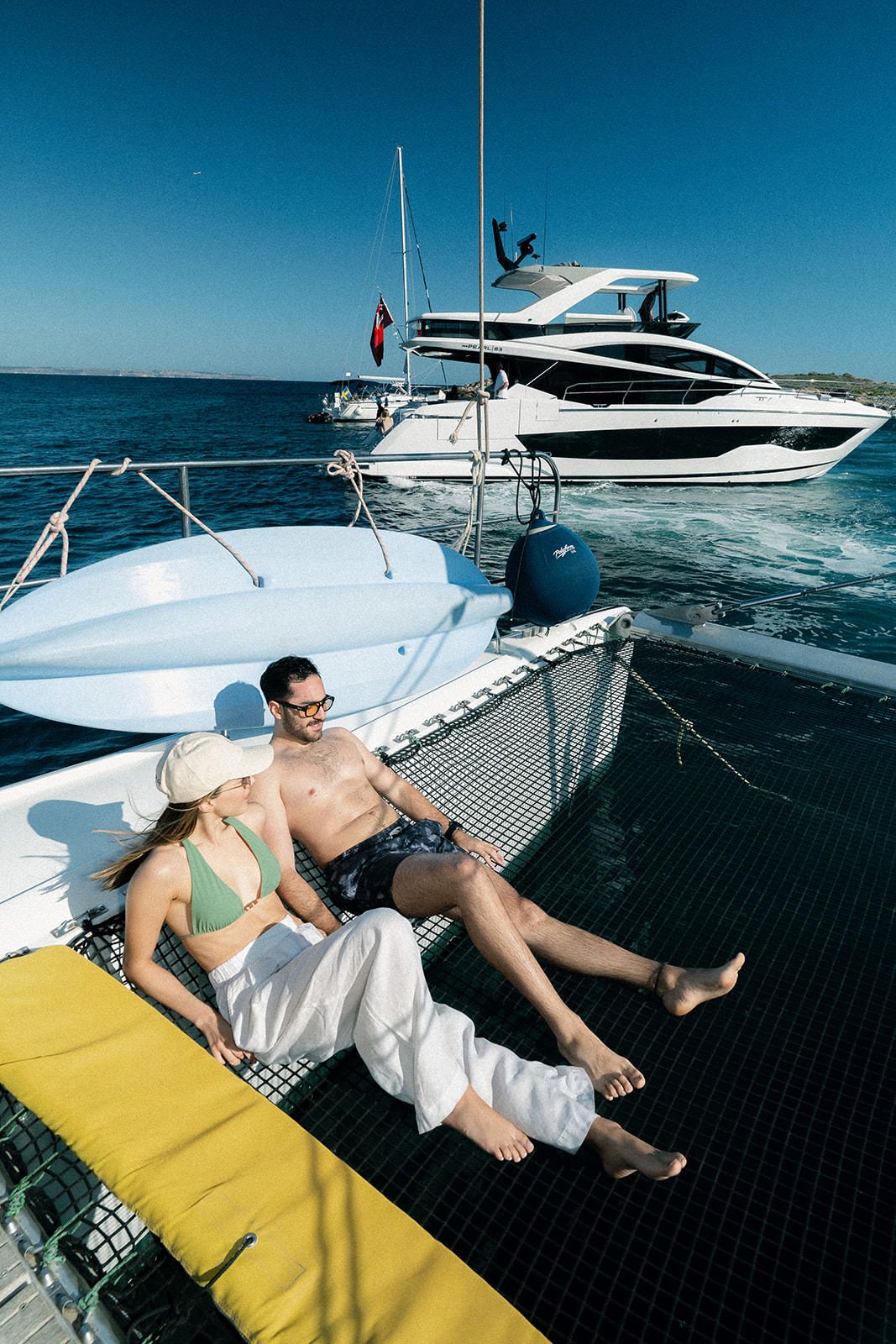 Luxury yacht cruising on blue ocean waters with people relaxing on deck nets under bright sunny skies.