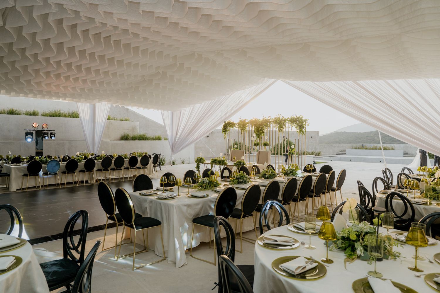 Luxurious wedding banquet hall with white ceiling draping, round tables, and lush green floral decor.