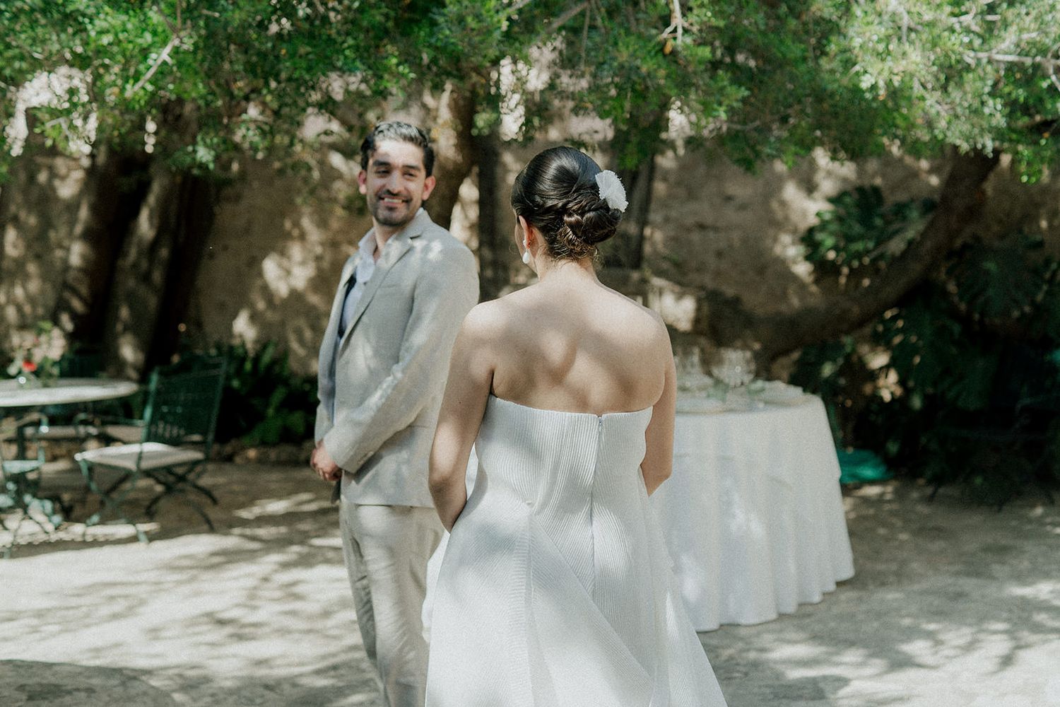 A couple in wedding attire dancing together in a sunlit garden setting.