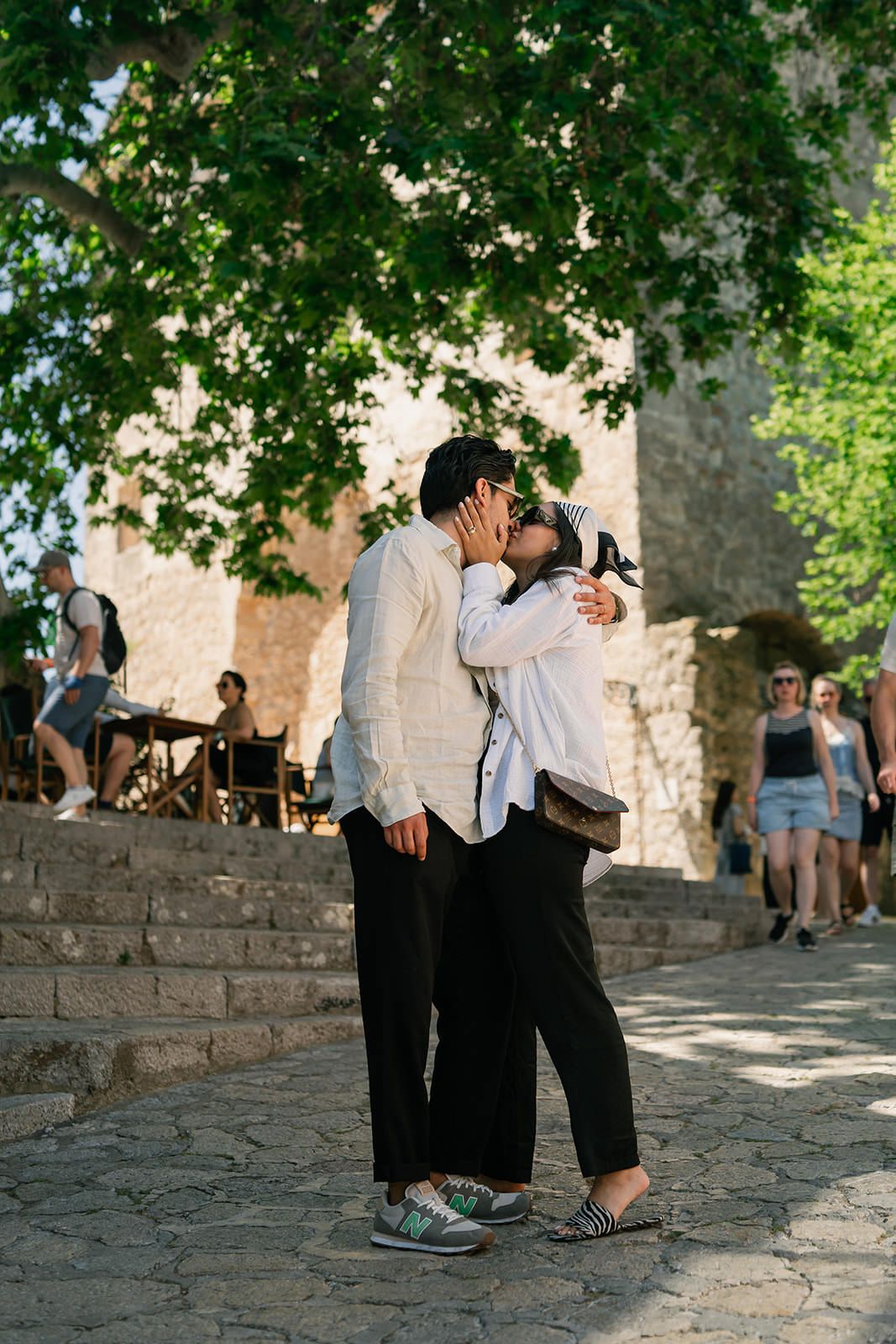 A couple shares an intimate moment on stone steps surrounded by green foliage and ancient architecture.