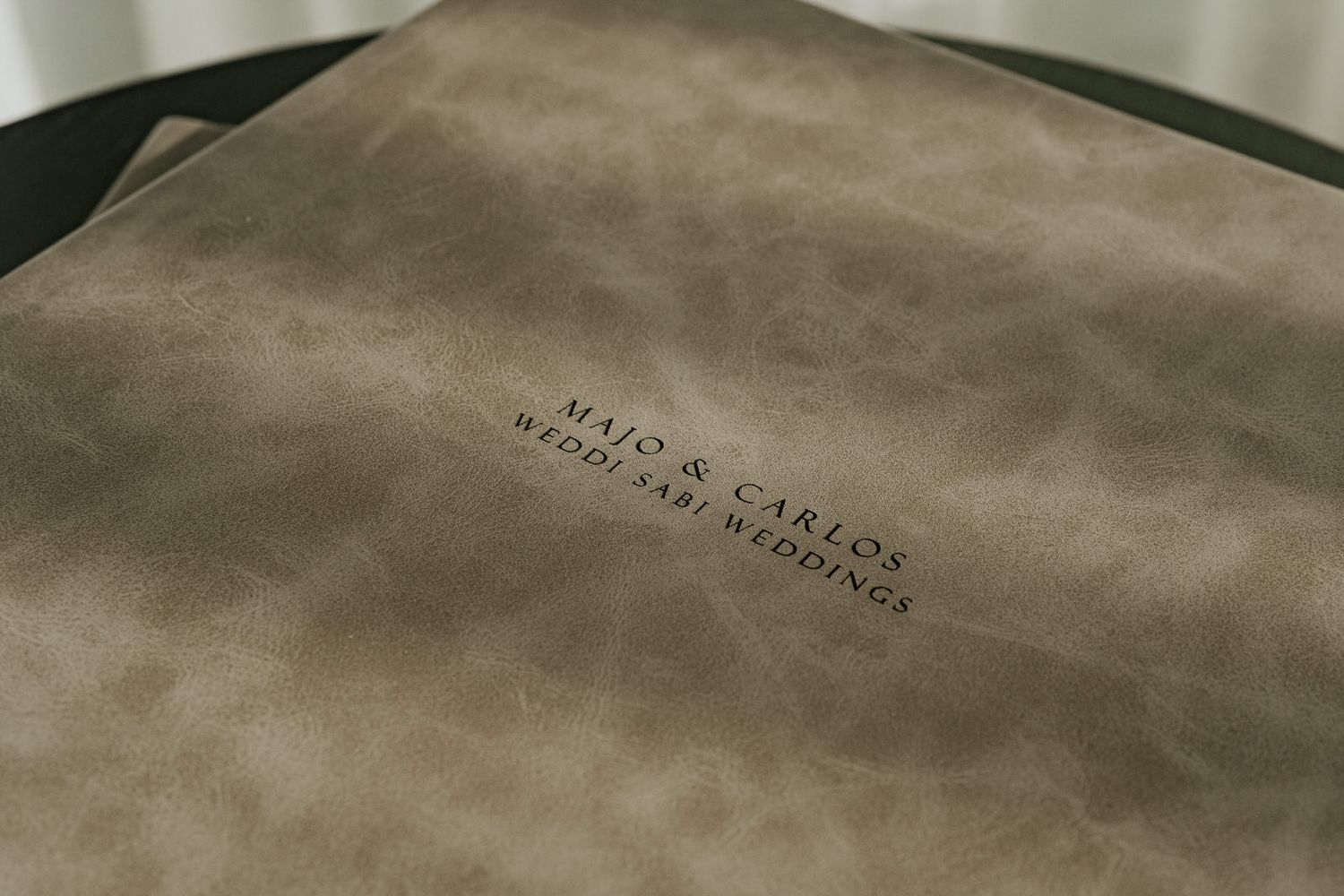 Close-up of a taupe suede wedding album embossed with Majo & Carlos destination wedding text.