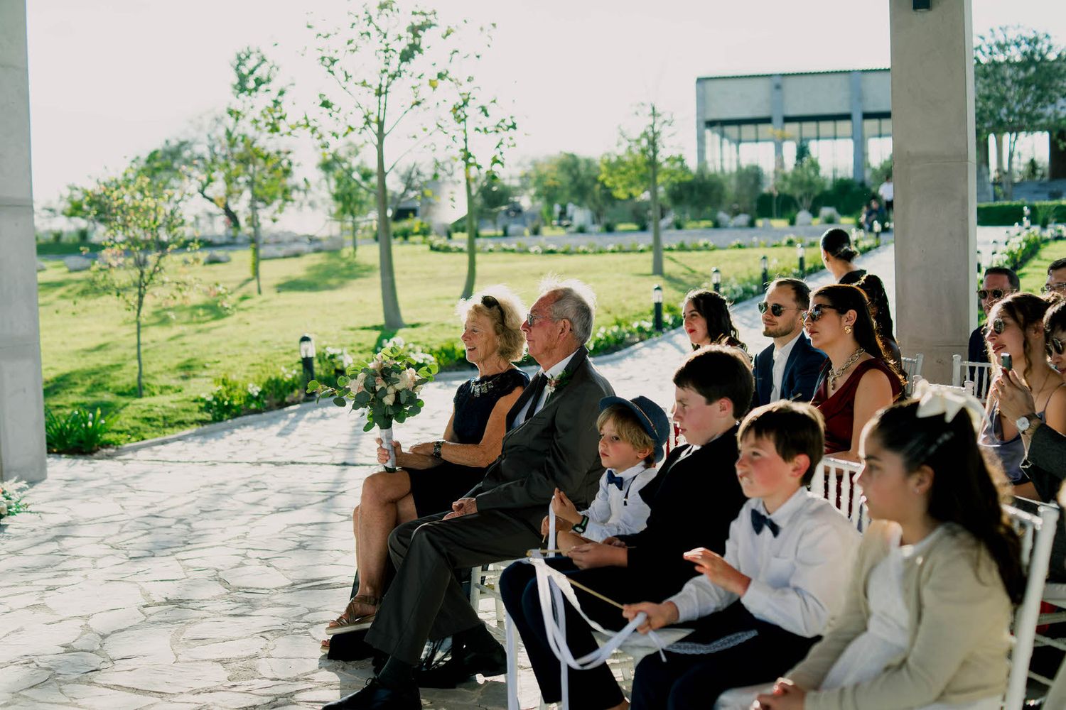 Wedding guests watching ceremony from seats in an outdoor covered venue.