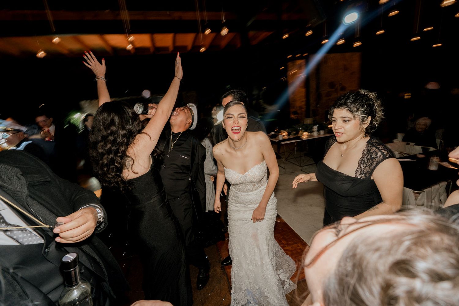 Guests dancing energetically at a wedding reception with colorful party lighting.