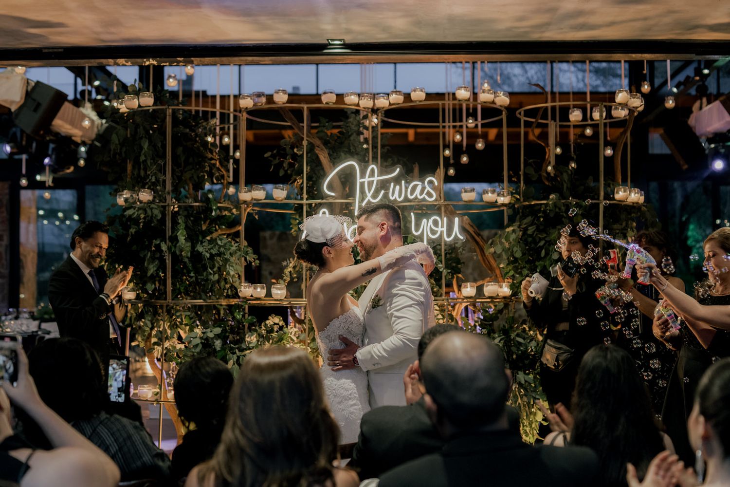 Wedding guests celebrate on a dance floor under twinkling lights at an evening reception.