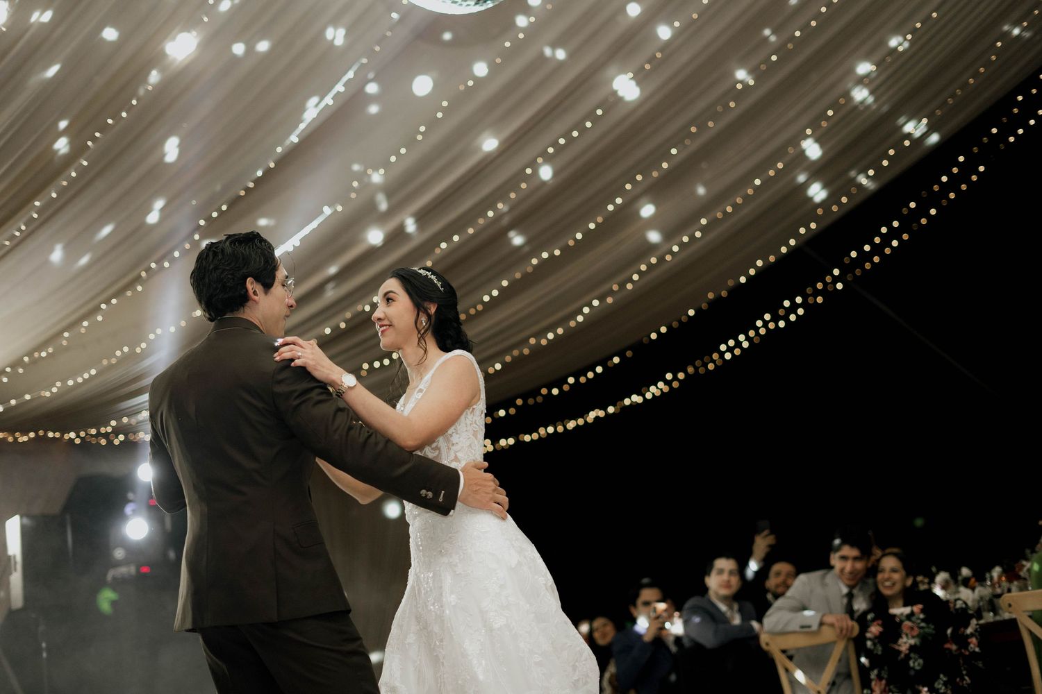 Wedding reception dance floor scene with romantic lighting and fabric ceiling decorations.