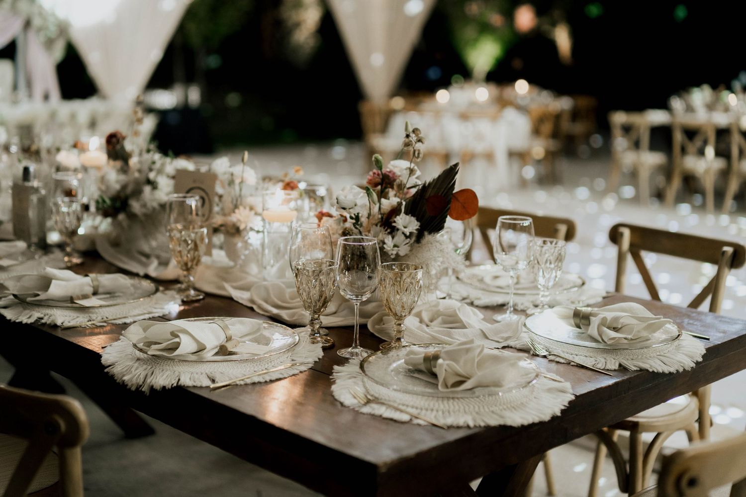 Long banquet tables set with elegant place settings under draped fabric and string lights.