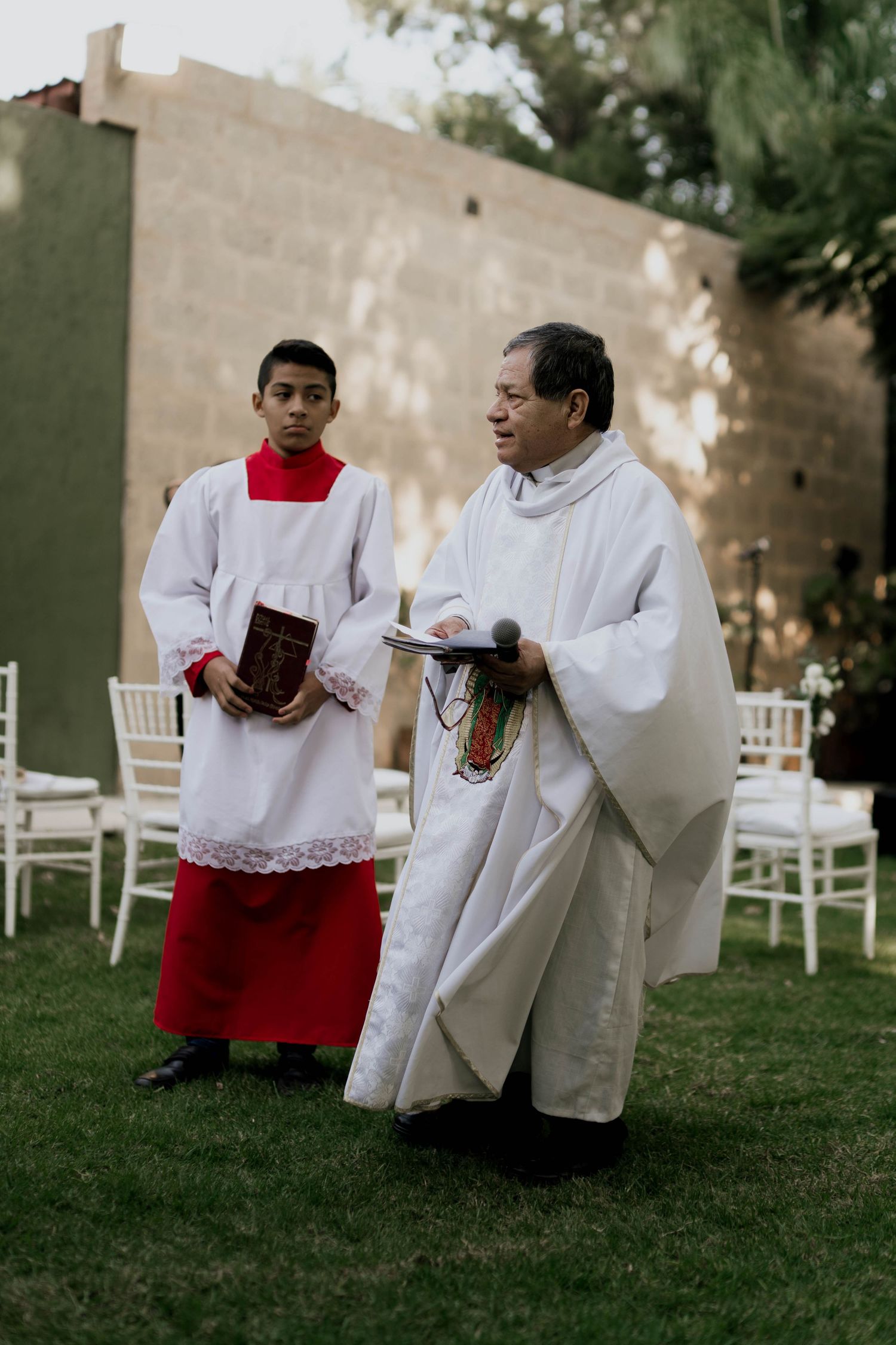 Altar servers in white robes preparing for a religious ceremony on grass.