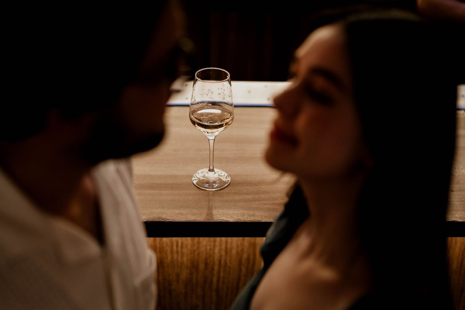 Wedding rings and wine glasses on dark wooden surface in intimate setting.