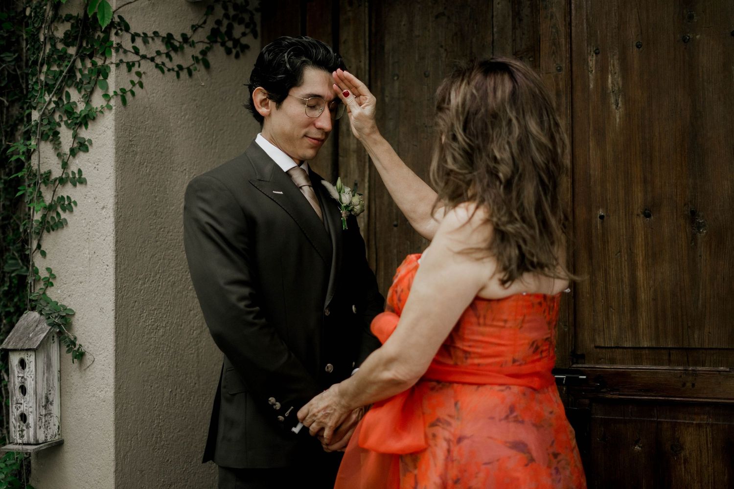 Romantic moment captured between couple in formal wear and orange dress against stone doorway.