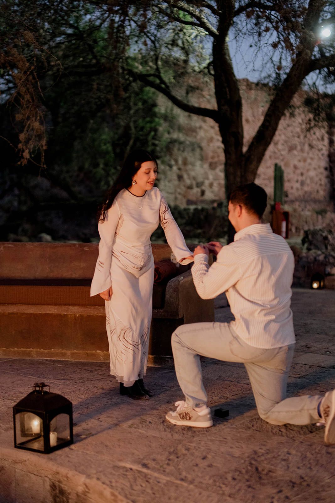 A romantic proposal moment unfolds on a stone patio at sunset.