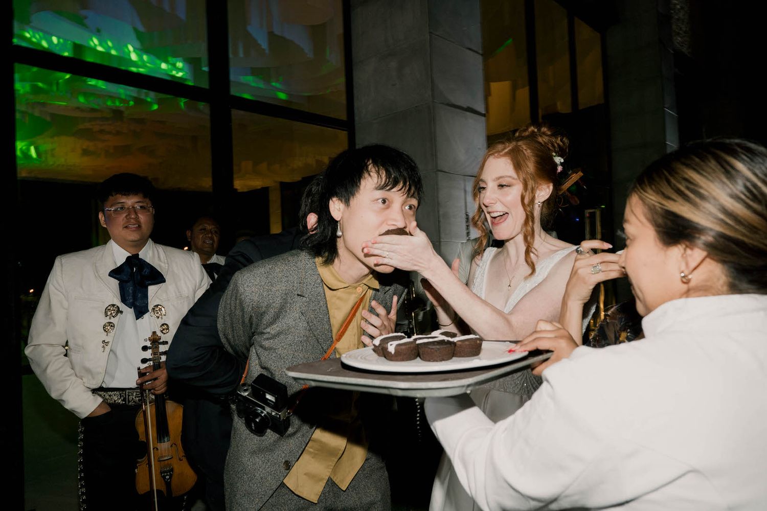Wedding reception party with green ambient lighting and guests dancing indoors.