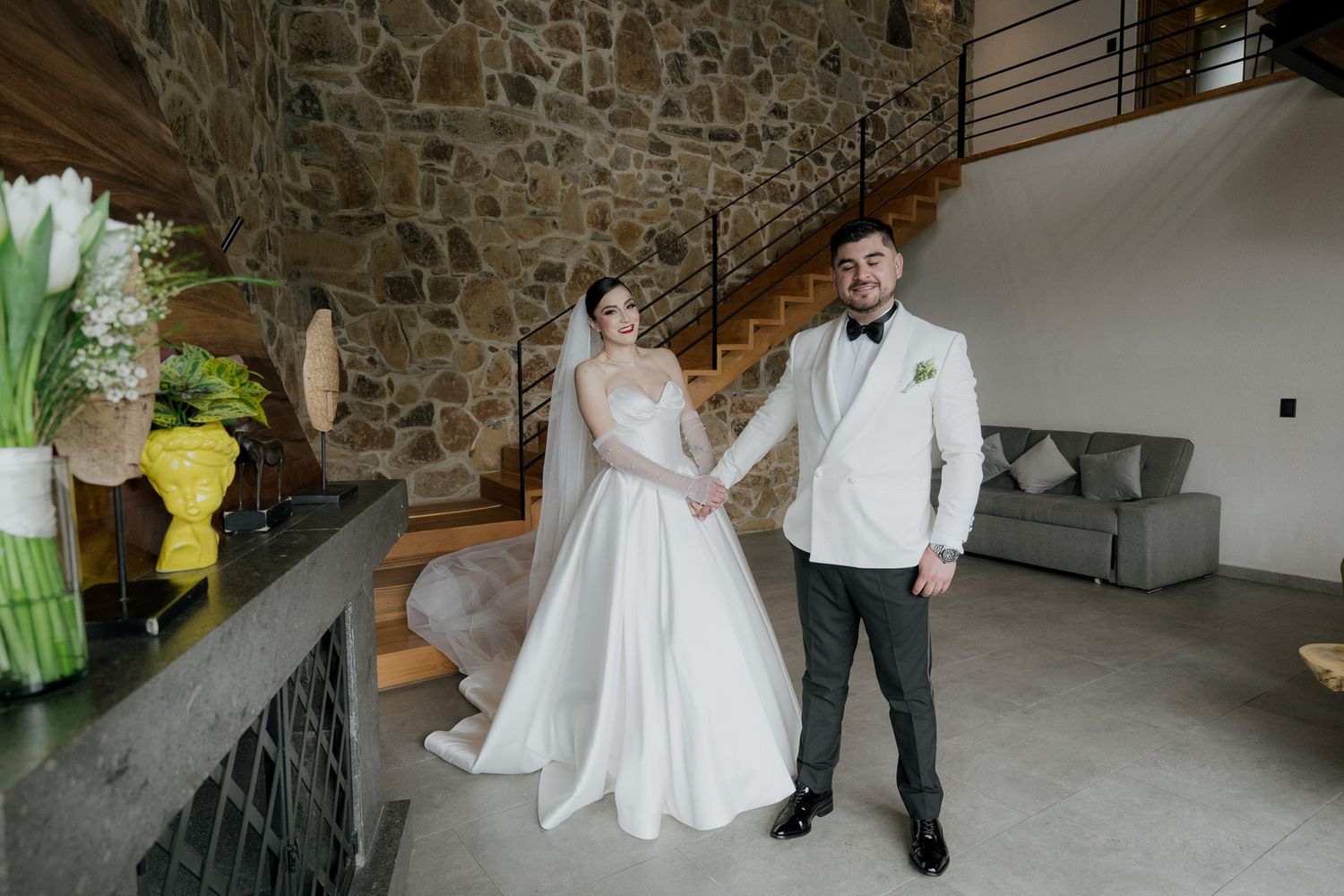 Elegant couple in white attire standing in modern stone-walled venue space.
