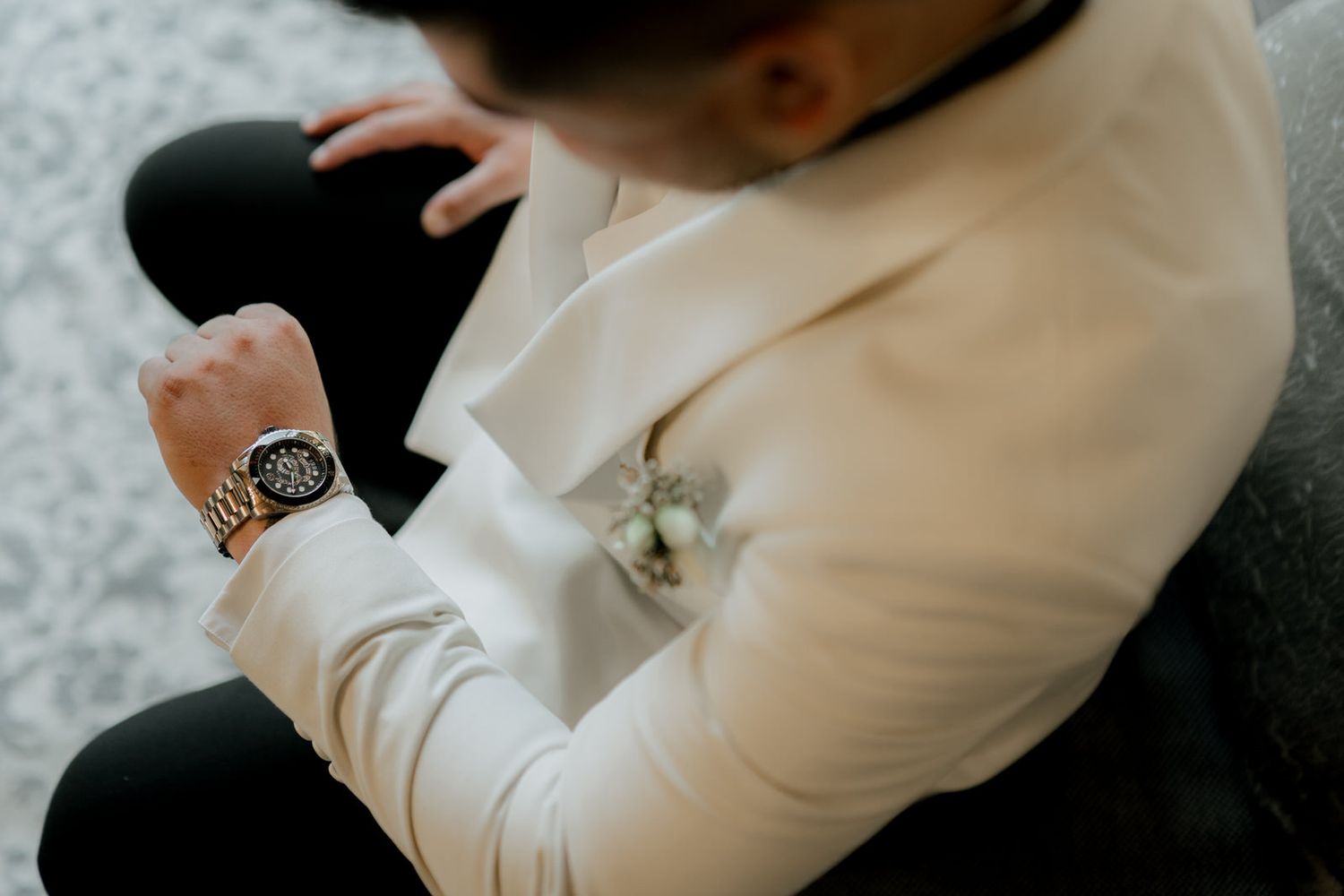 Detail shot of wristwatch and white formal jacket sleeve against grey carpet.
