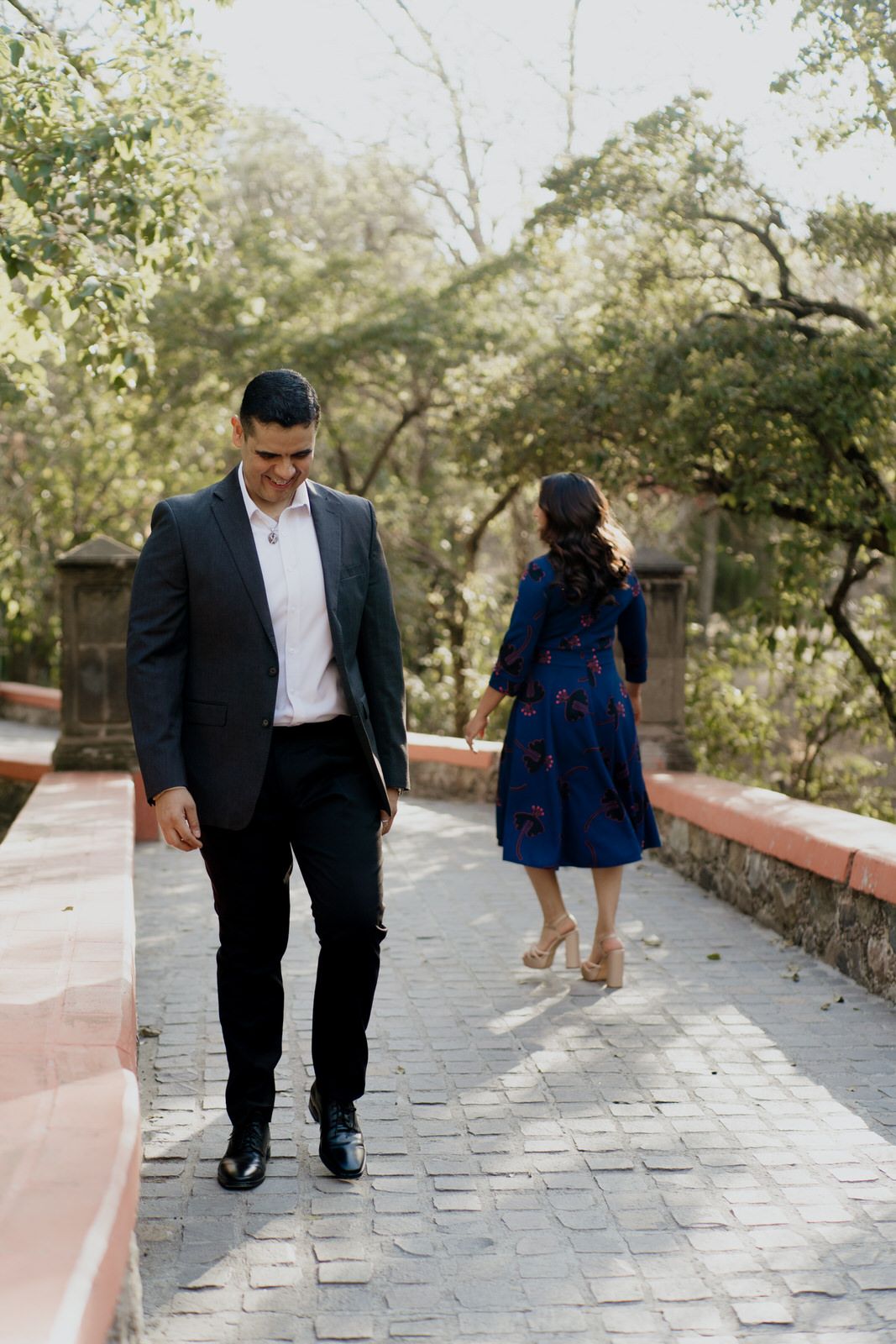 A couple walks together on a stone pathway surrounded by trees and greenery.