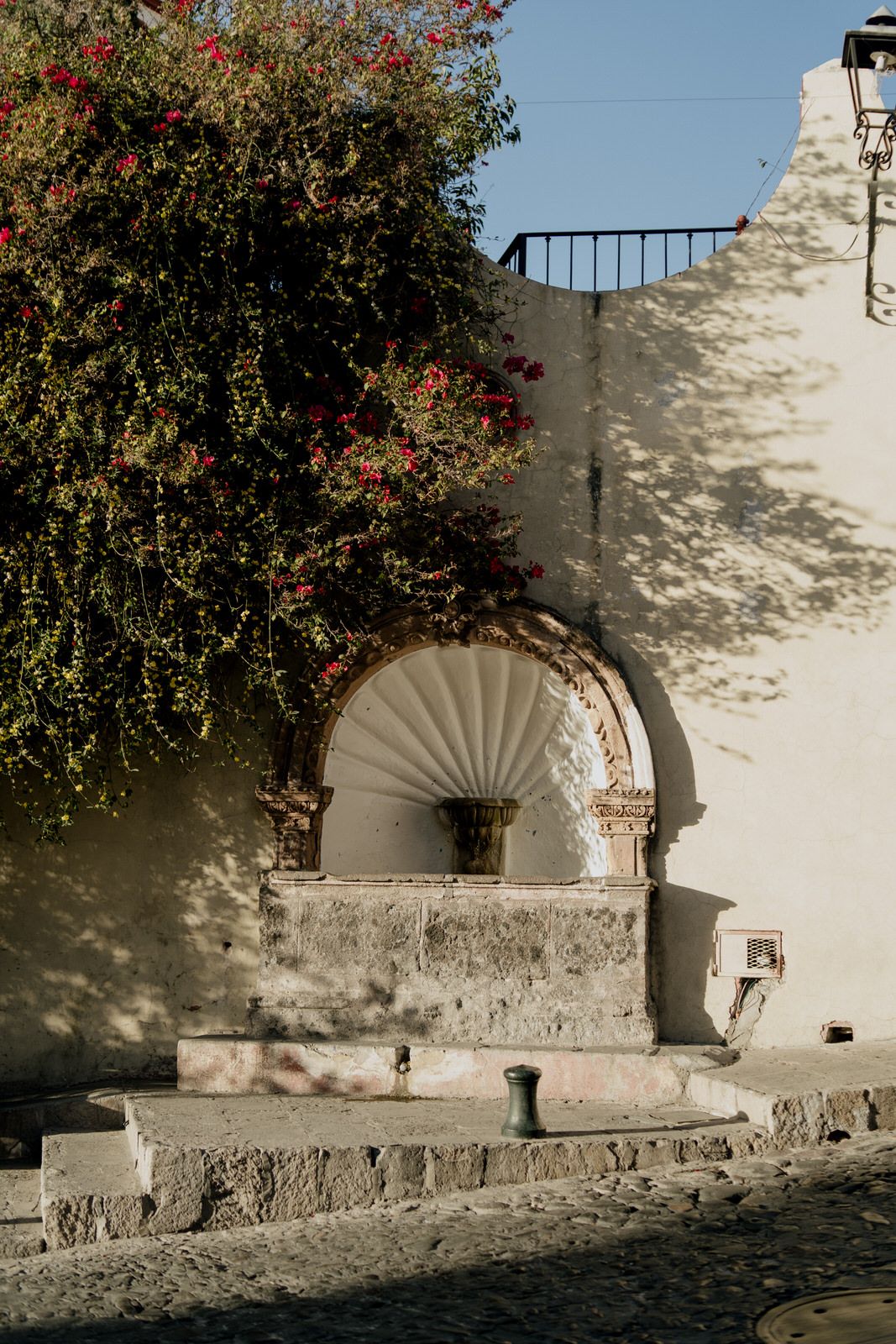Stone archway with flowering vines creates a romantic frame against white colonial architecture.