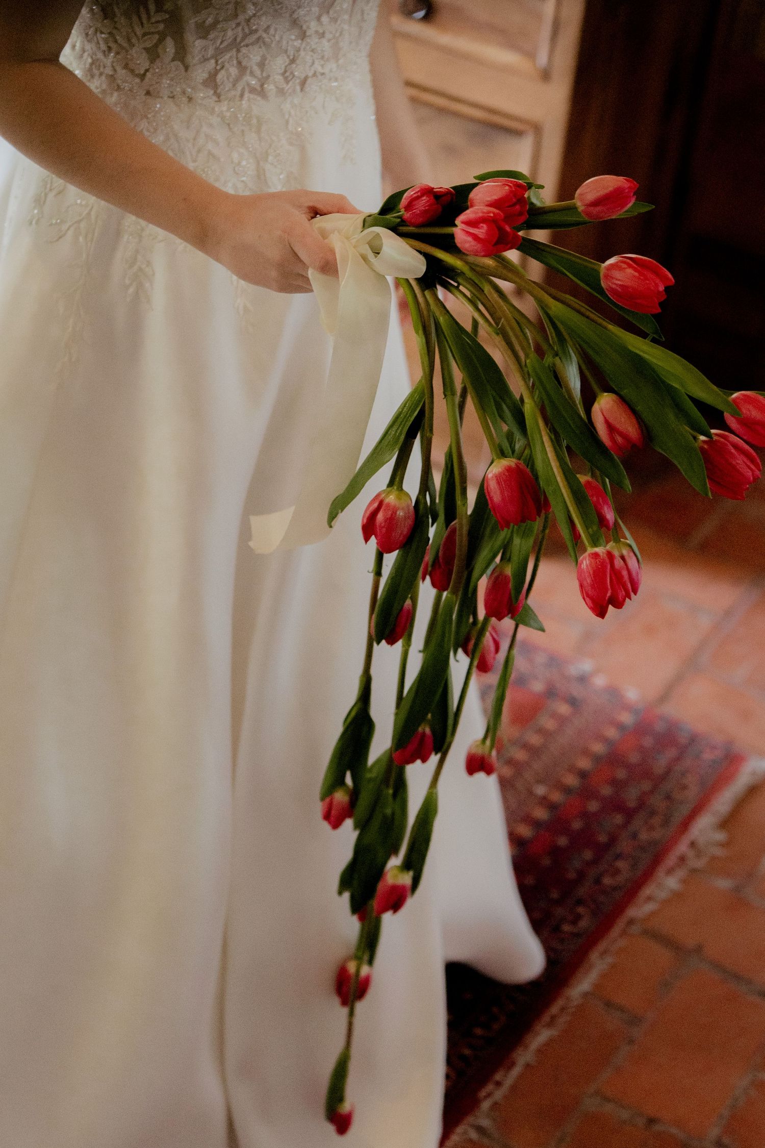 Red tulips cascade elegantly against a white curtain background creating a romantic wedding detail.