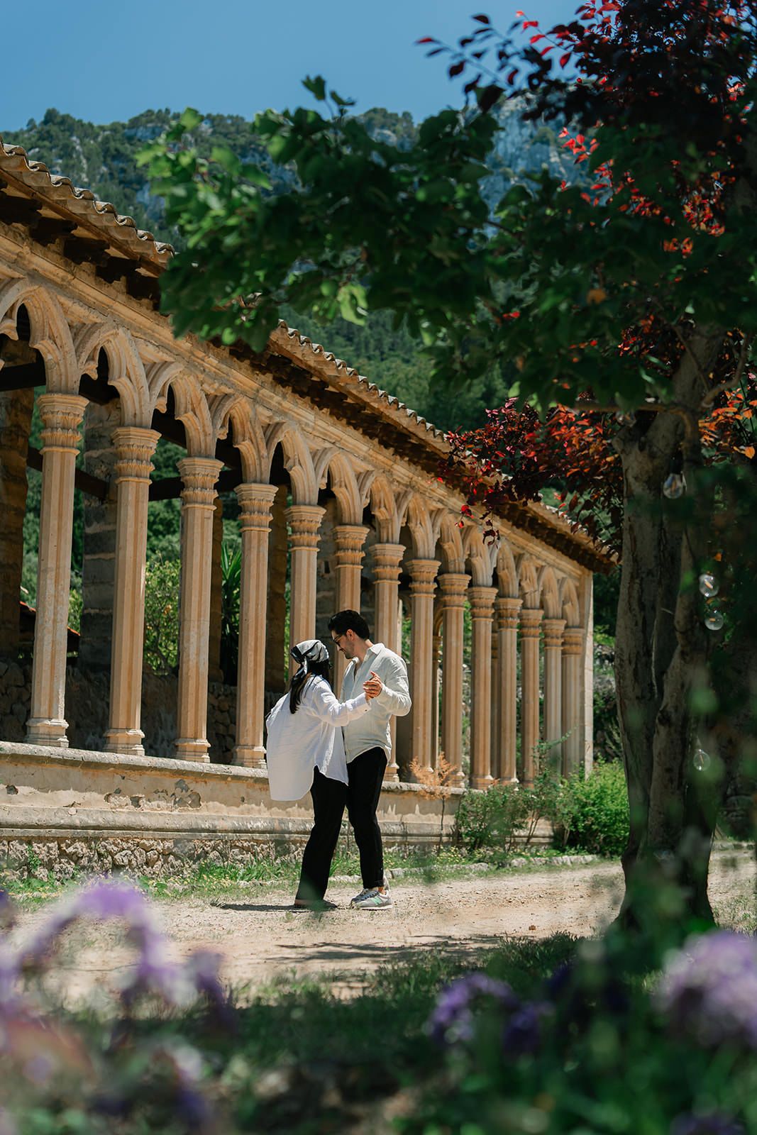 Beautiful stone colonnade with arched pillars in a garden setting creates a romantic walkway framed by blooming flowers.