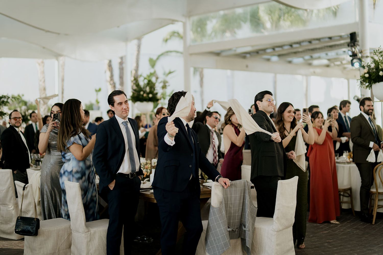 Wedding guests raising glasses for a toast at an elegant outdoor reception under a white canopy.