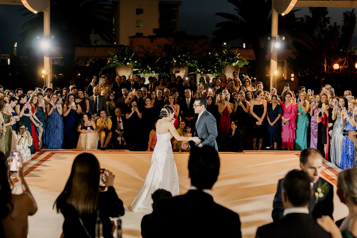 Bride and groom share first dance outdoors surrounded by cheering wedding guests at elegant evening reception.