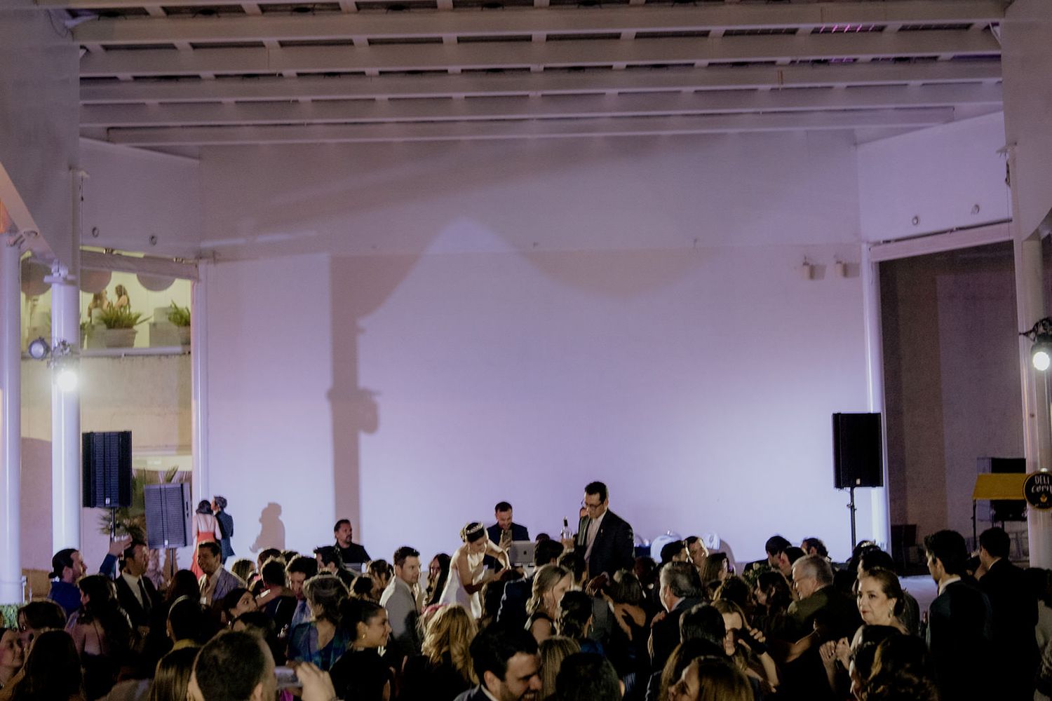 Guests fill a elegant white venue during a wedding reception with live band performance on stage.
