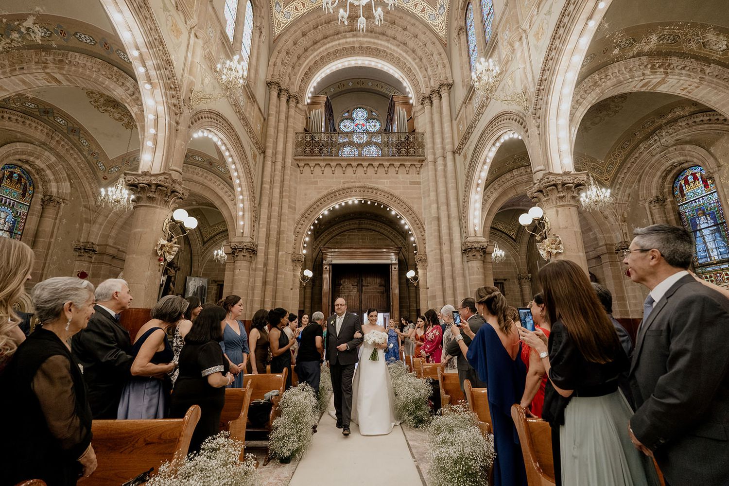 Bride and groom walk down the aisle of an ornate cathedral church surrounded by wedding guests.