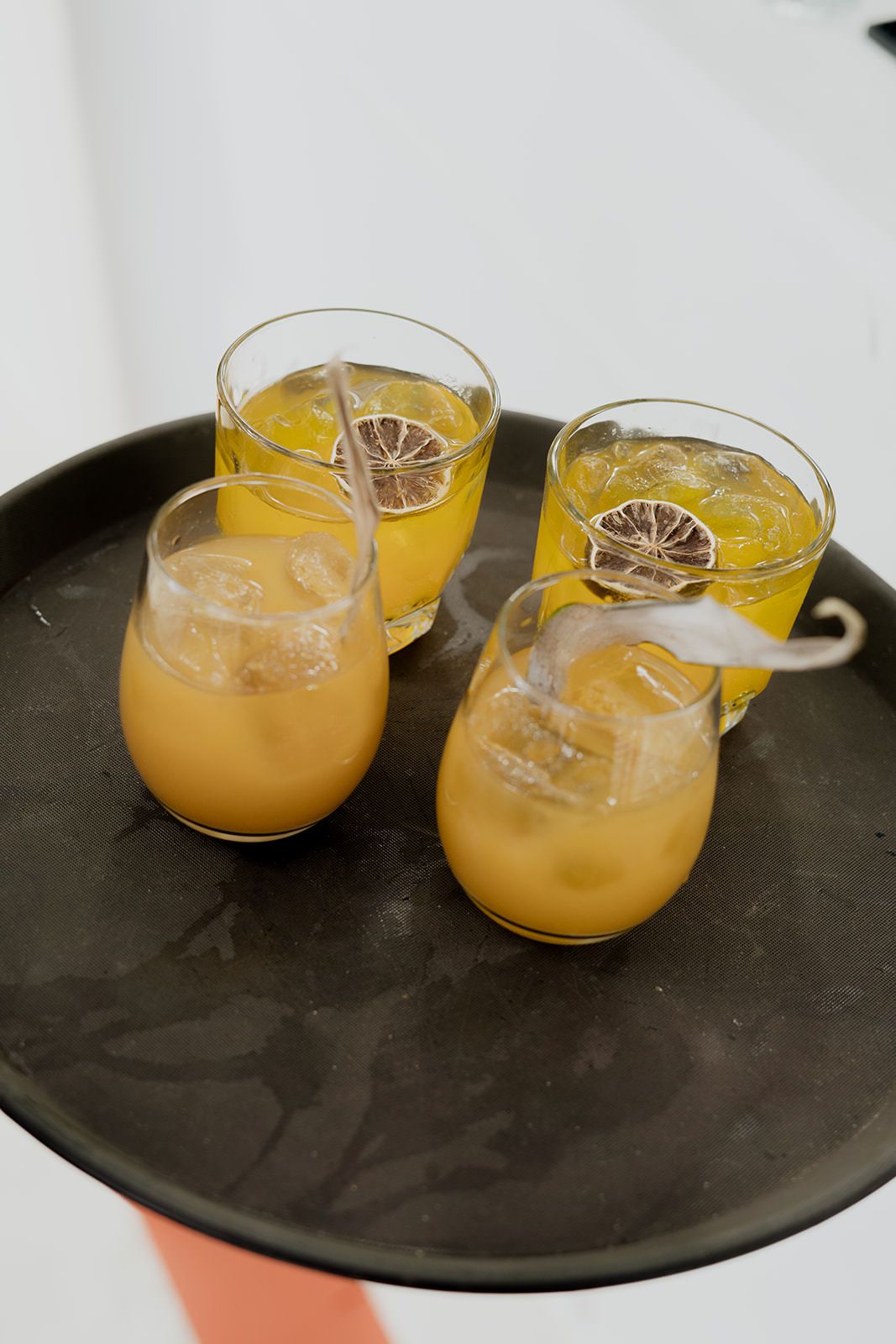 Four glasses of iced orange juice garnished with dried citrus slices on a dark serving tray.