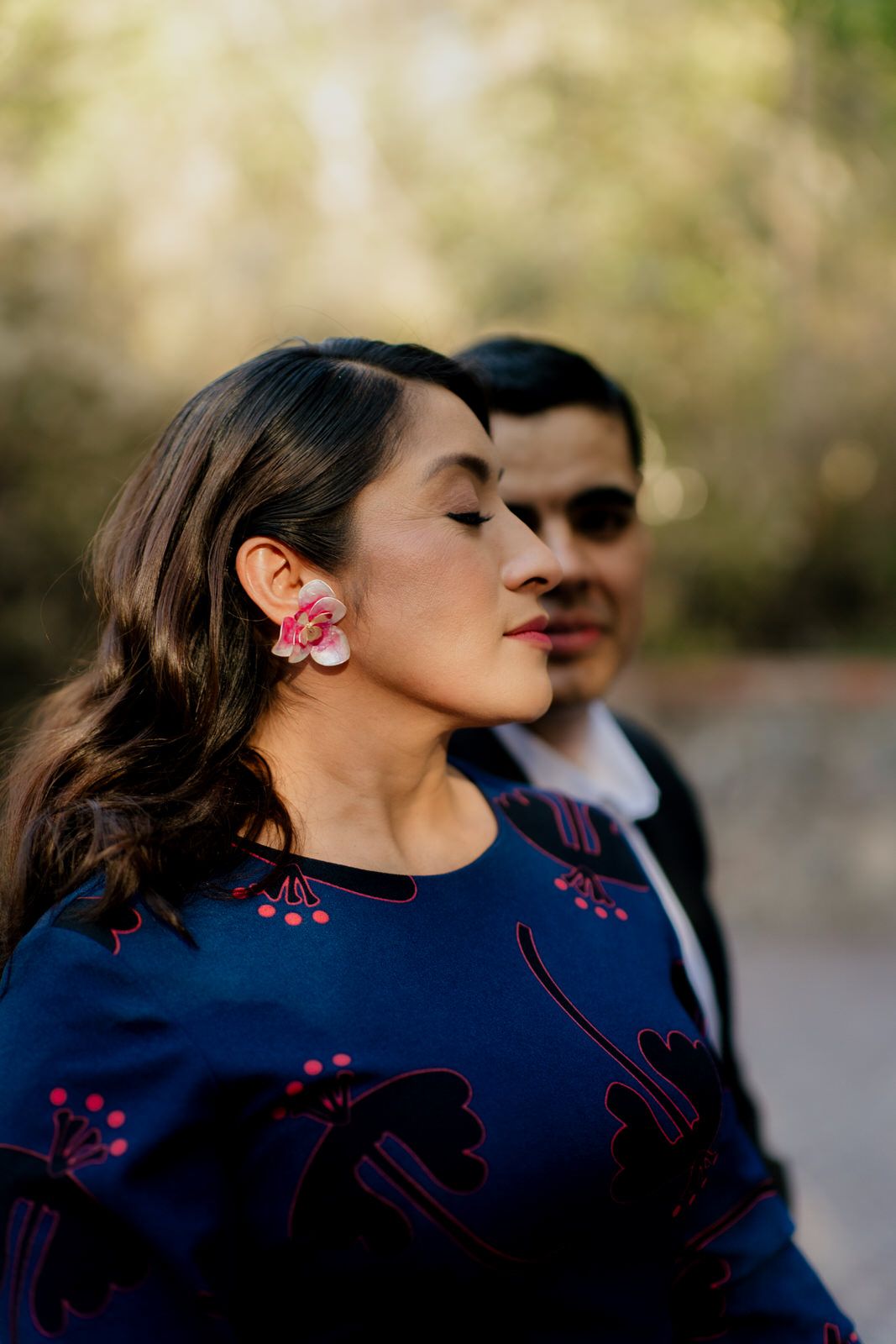 Romantic couple in blue dress and suit embracing against a natural outdoor backdrop.