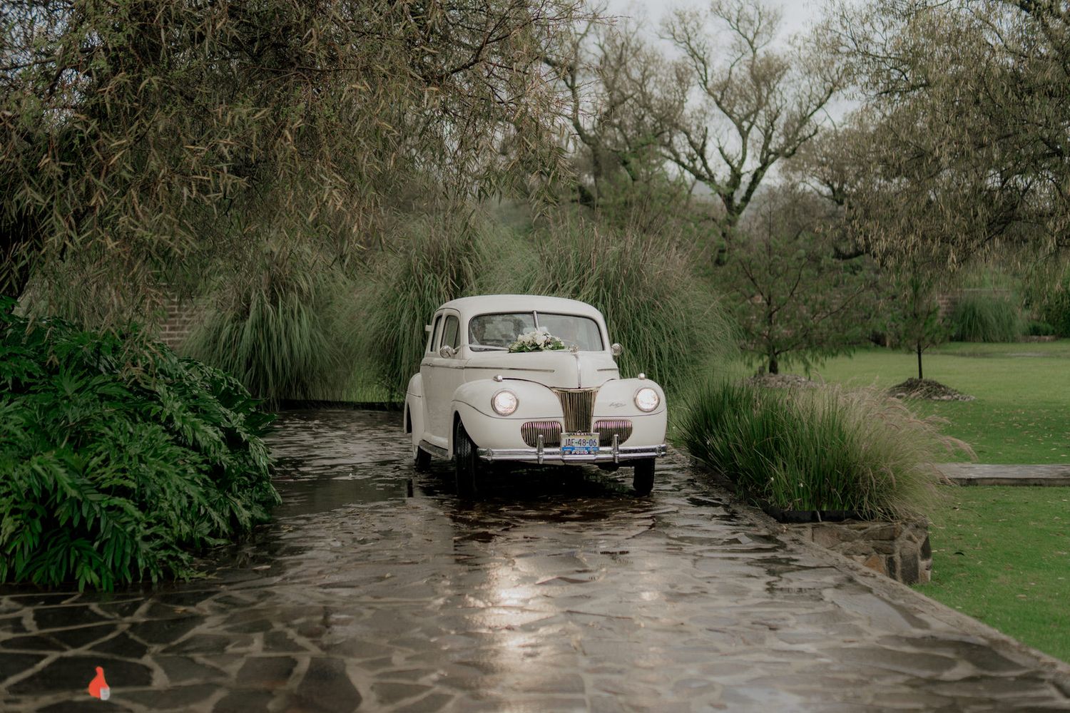 Classic white vintage car parked along a stone pathway surrounded by greenery.