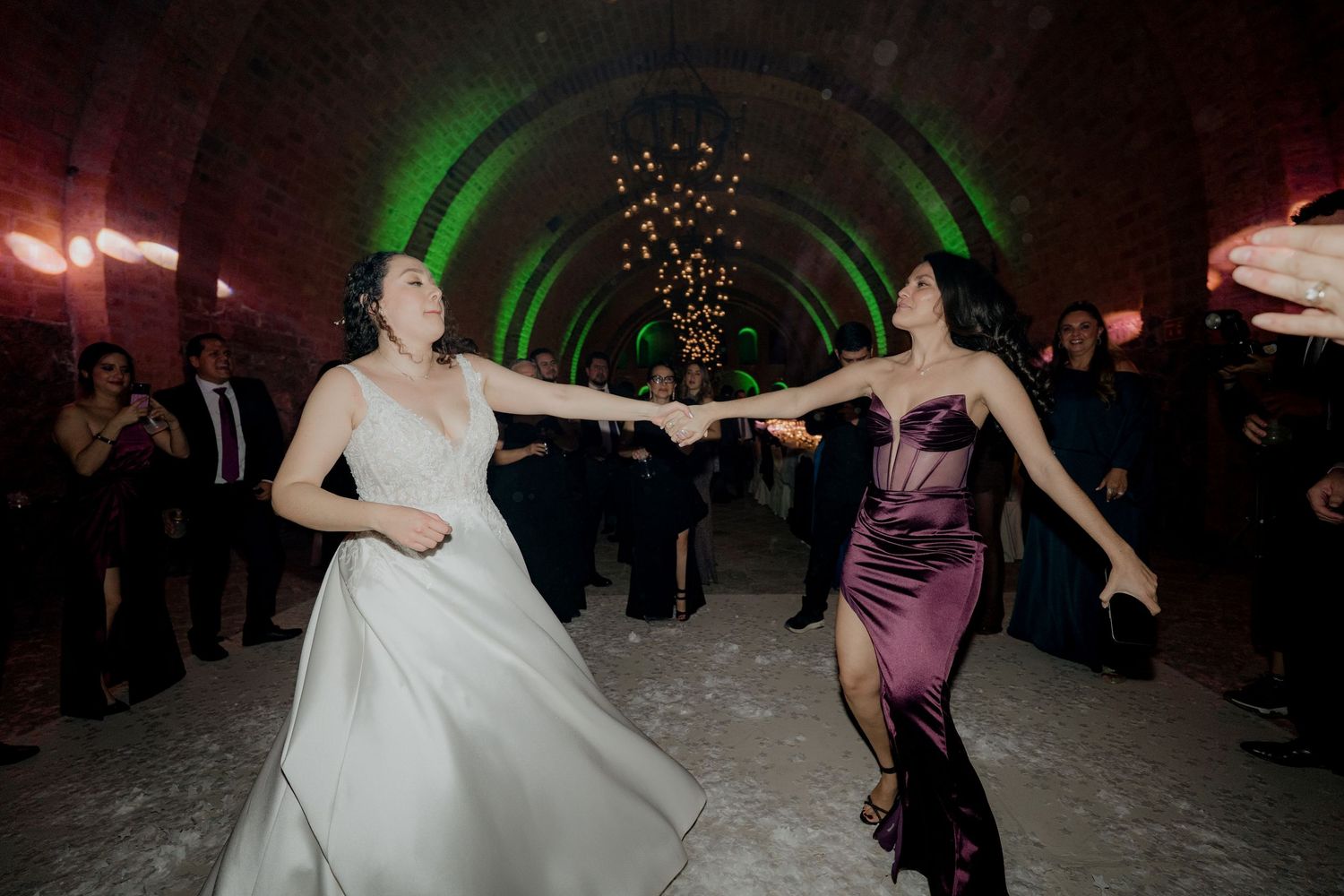 Two people dance energetically in an arched brick venue with festive lighting.