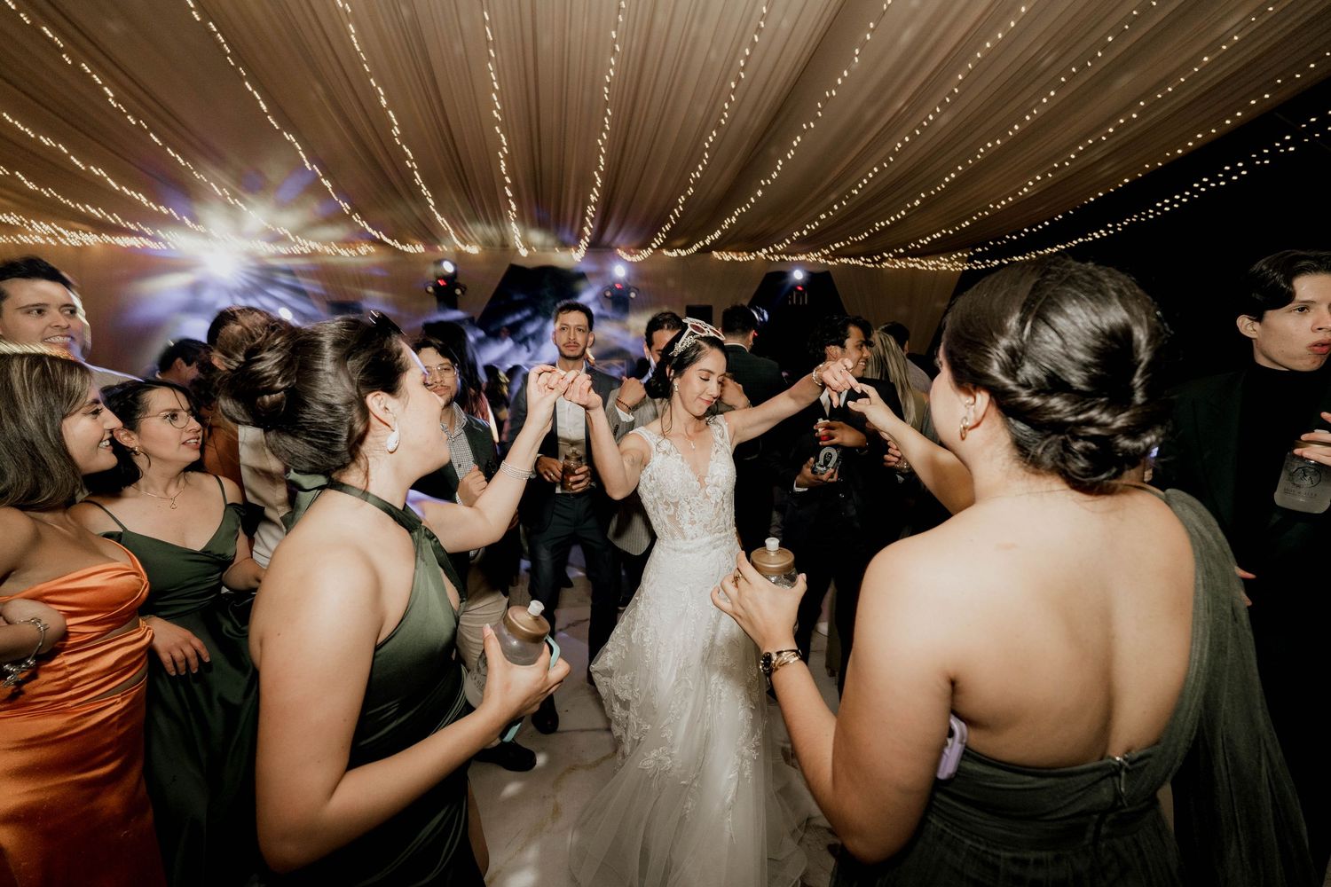 Wedding celebration with guests dancing under illuminated tent ceiling with fabric swags.