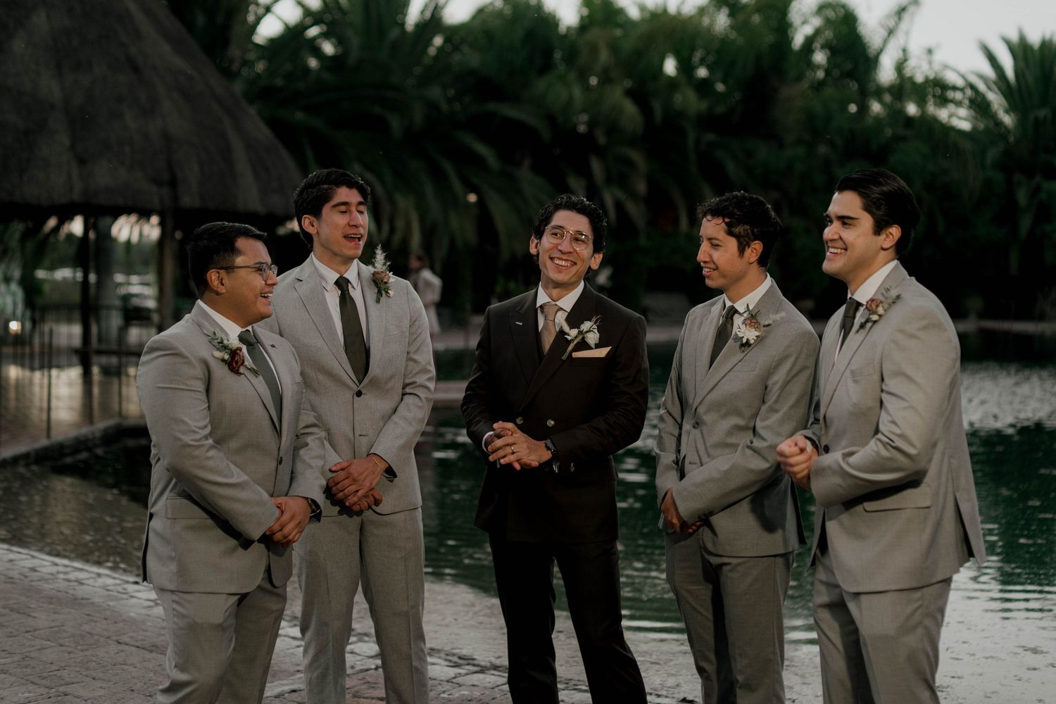 Group of men in gray suits laughing together during an outdoor wedding celebration.