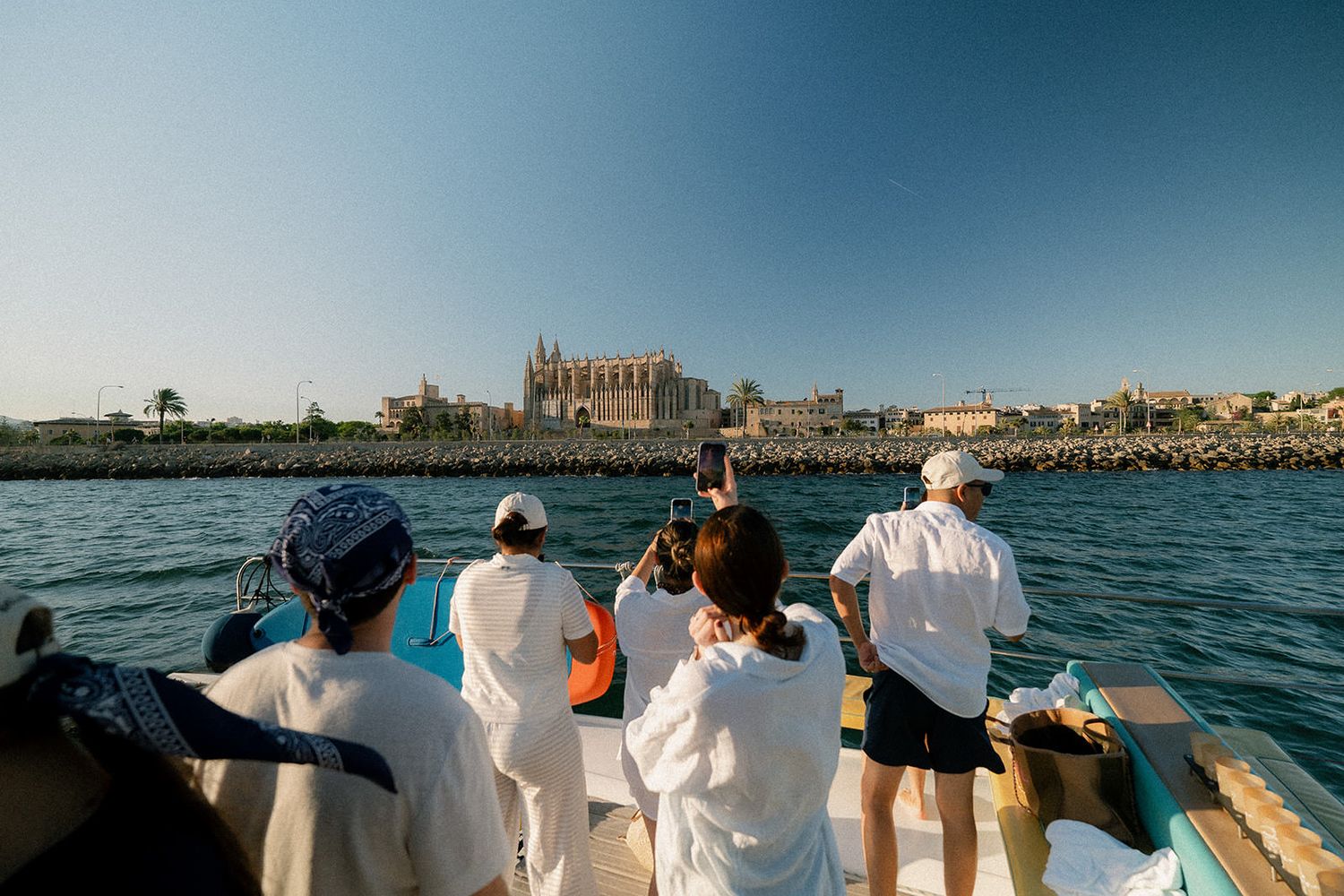 A group of tourists on a boat tour admiring the historic skyline of Palma de Mallorca, Spain from the Mediterranean Sea.