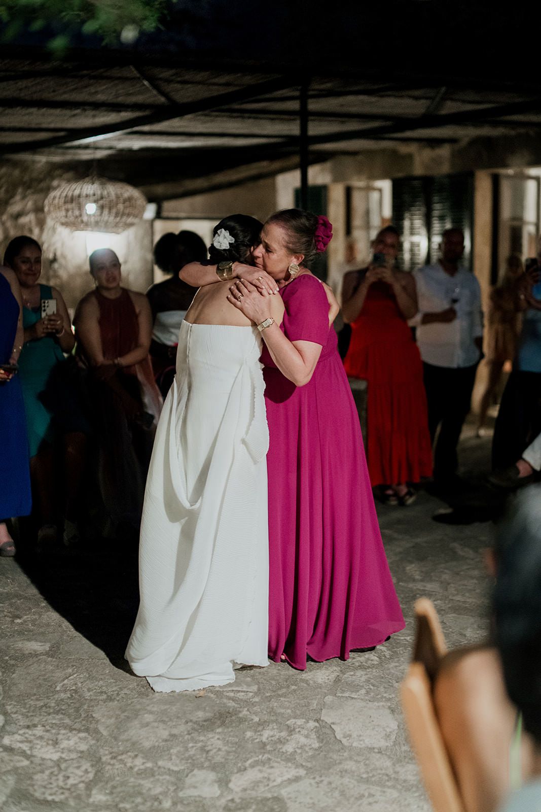 Wedding party members in white and magenta dresses dance together on a stone floor at an indoor reception.
