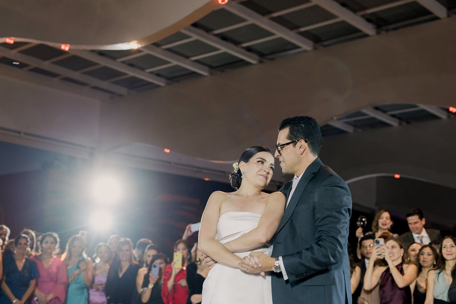 Bride and groom share romantic first dance surrounded by guests at wedding reception.