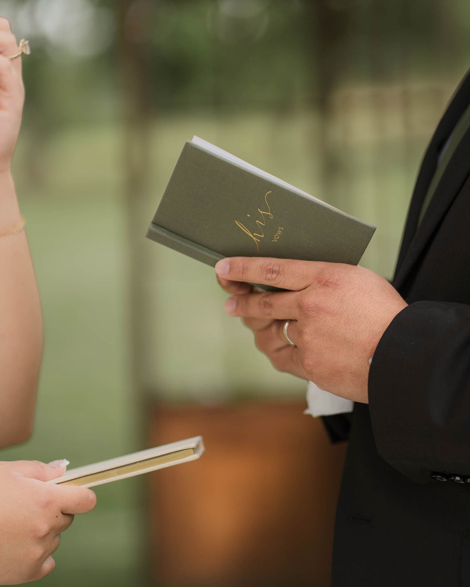 Bride and groom exchanging wedding vows while holding personalized vow booklets during outdoor ceremony.