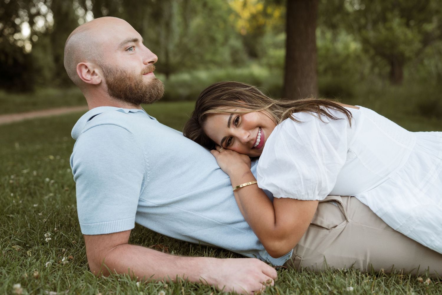 Couple relaxing on green grass in a park, woman smiling and resting her head on man's chest.