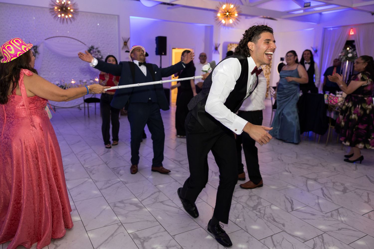Man dancing energetically at a wedding reception on a white marble dance floor surrounded by guests.
