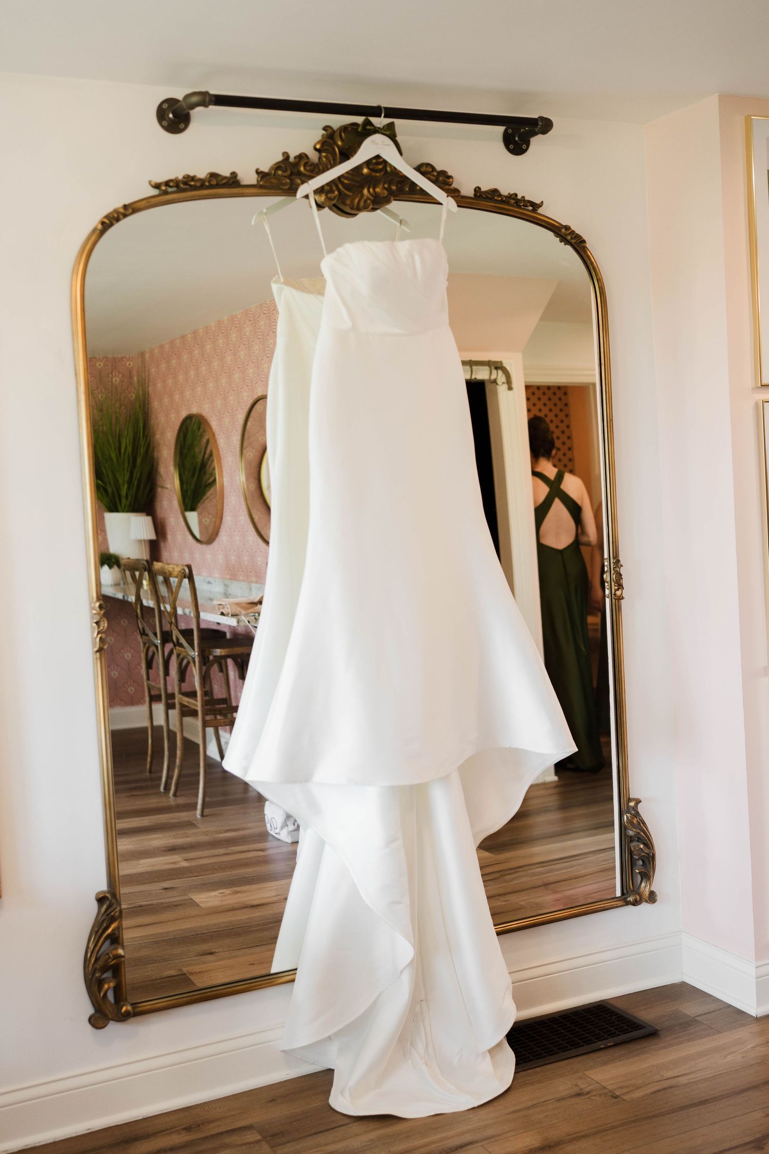 Elegant white strapless wedding gown with layered skirt hanging on a gold ornate mirror.