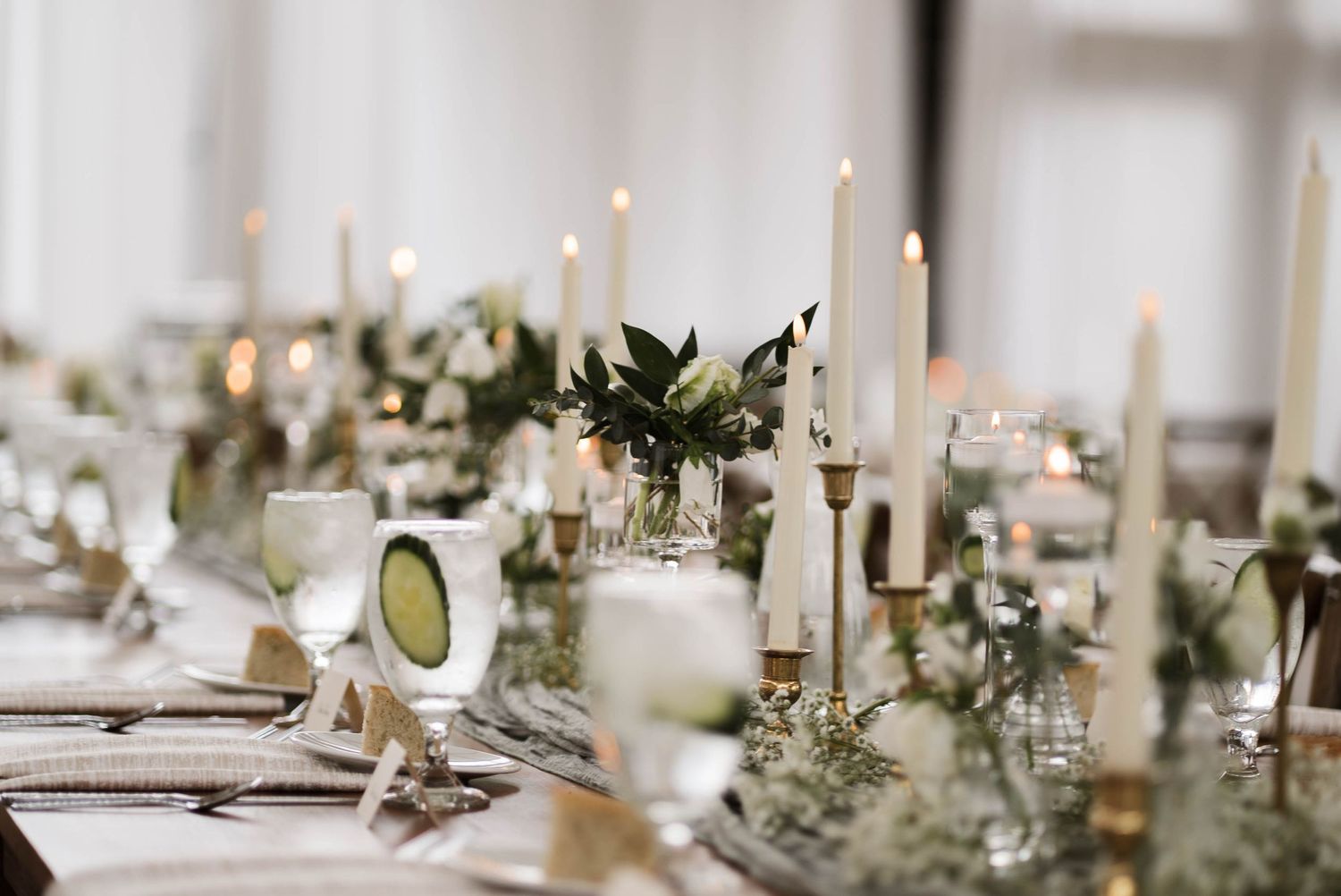Elegant wedding reception table with tall taper candles, greenery, and gold accents along a long banquet table.